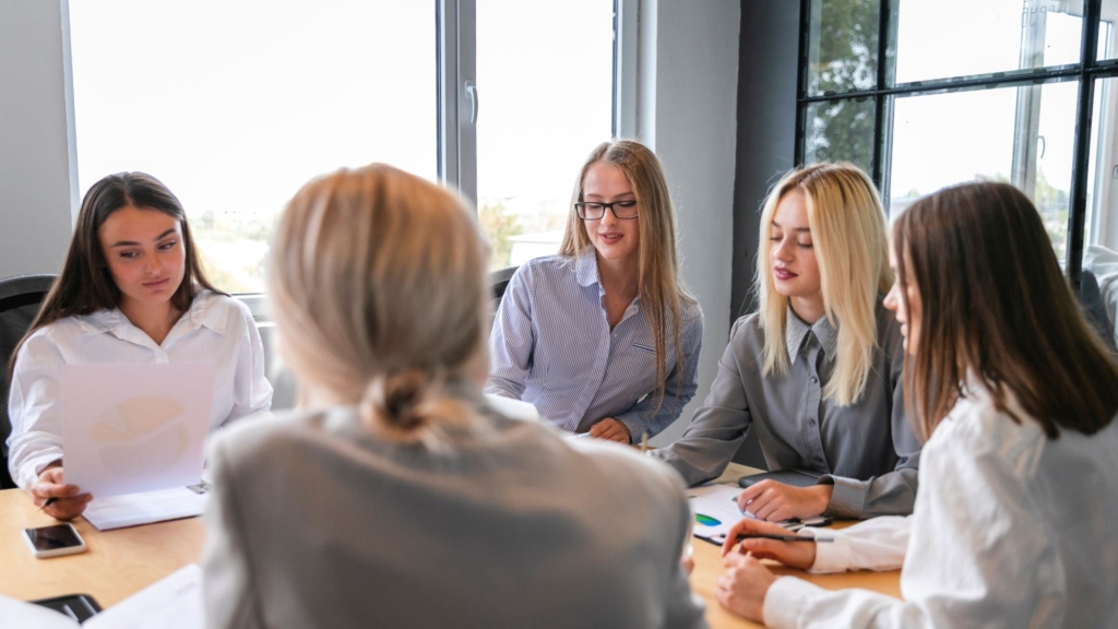 Reunião de negócios com liderança diversificada, onde várias mulheres estão liderando a discussão e tomando decisões estratégicas.